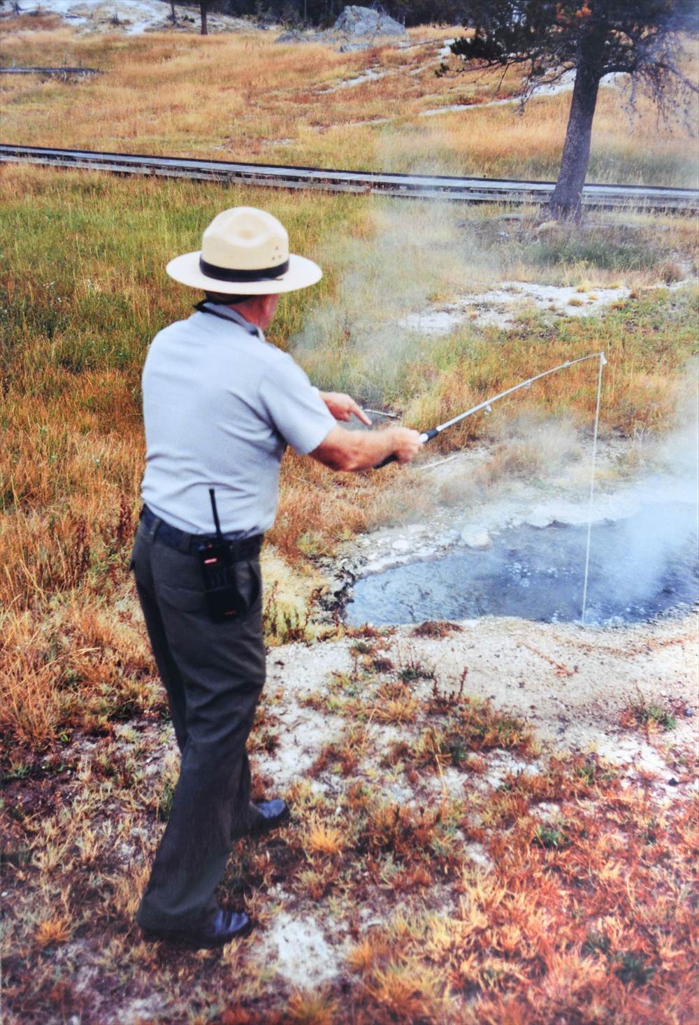 Picture of a ranger measuring the temperature of a hot spring using a fishing rod - like thermometer