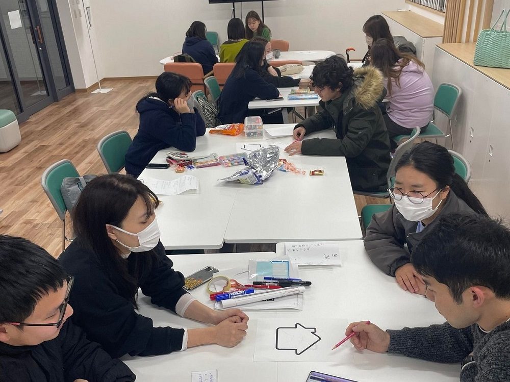 テーブルを囲んで学生たちが日本語ハウスロゴのアイディアを出し合う様子の写真