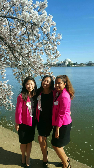 親善大使のジャケットとリボンを身に付け、満開の桜の下でポトマック川を背景に他のメンバーと記念撮影（左端が中原さん）
