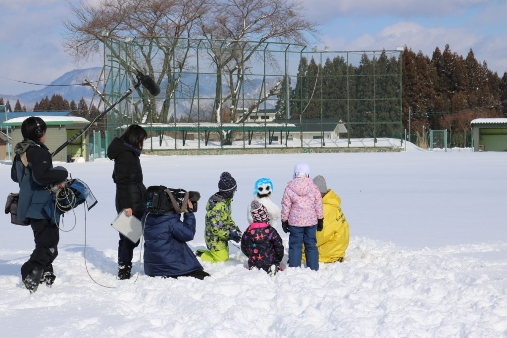 留学生と児童が共に雪像作りに挑戦している様子の取材風景