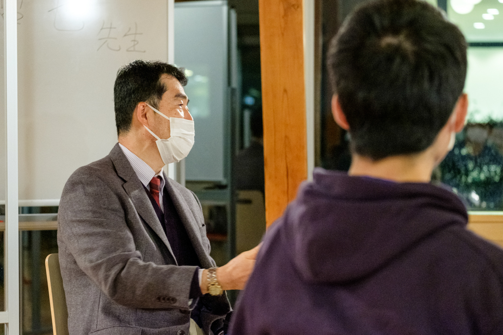 マイクを片手に、ファシリテーターとして豊田教授に質問する磯貝副学長の写真