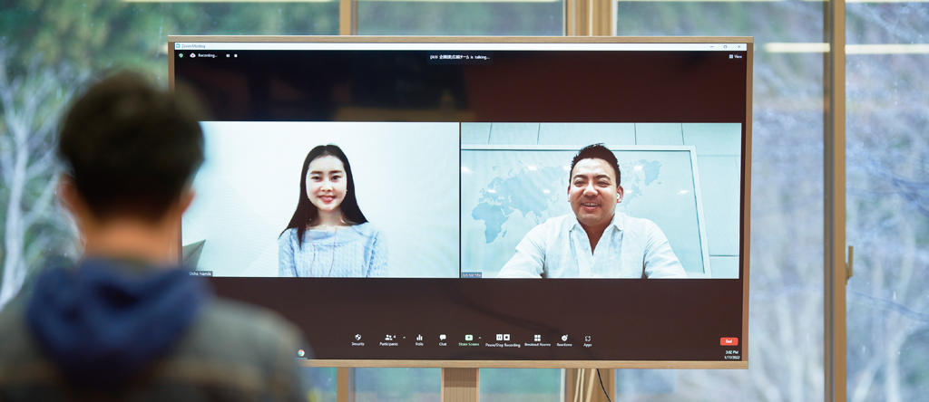 ビデオ通話でオンライン参加した卒業生2人が画面に大型モニターに映っている写真