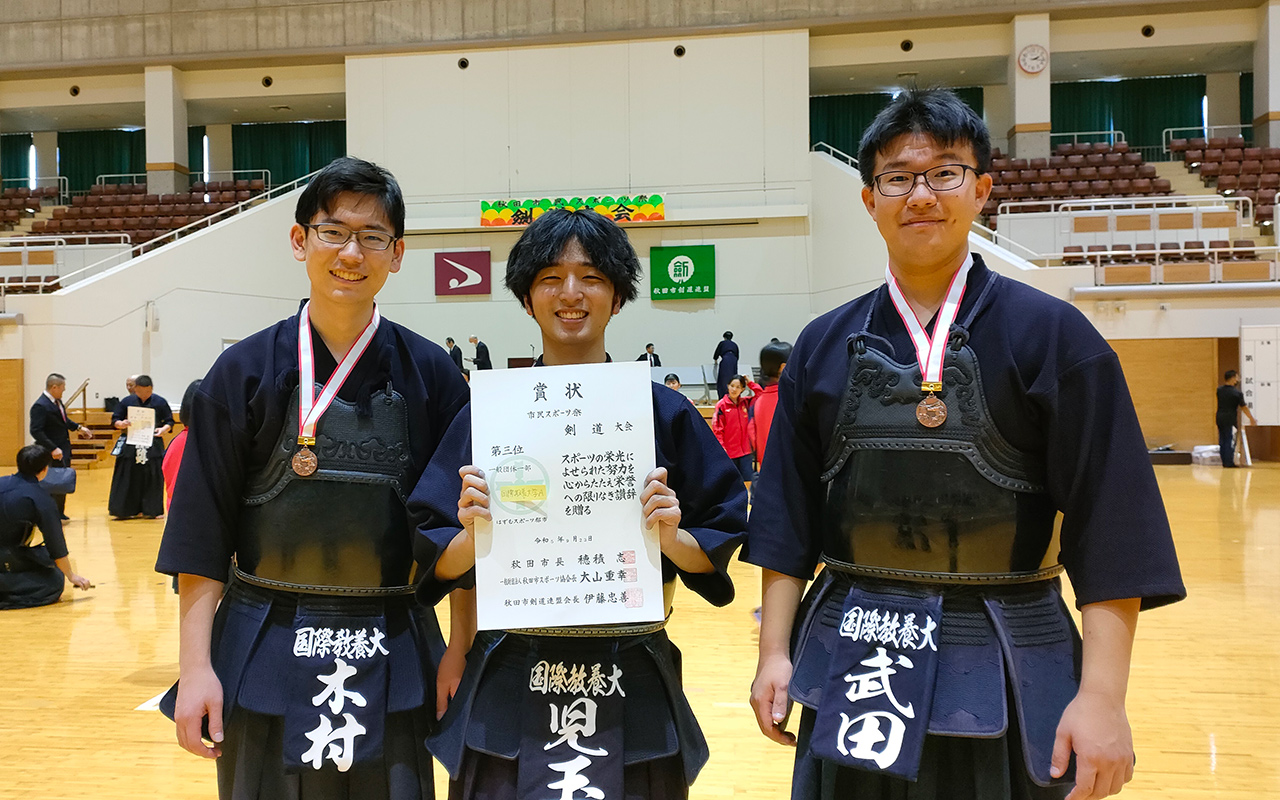 大会で入賞した3名の学生が賞状を持って微笑んでいる写真